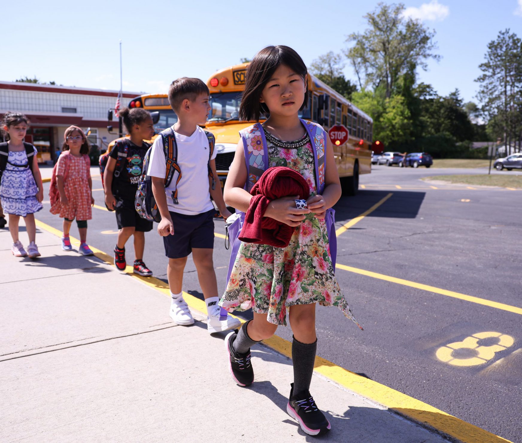 Student smiling while holding supplies. She is walking into her class on the first day of school.