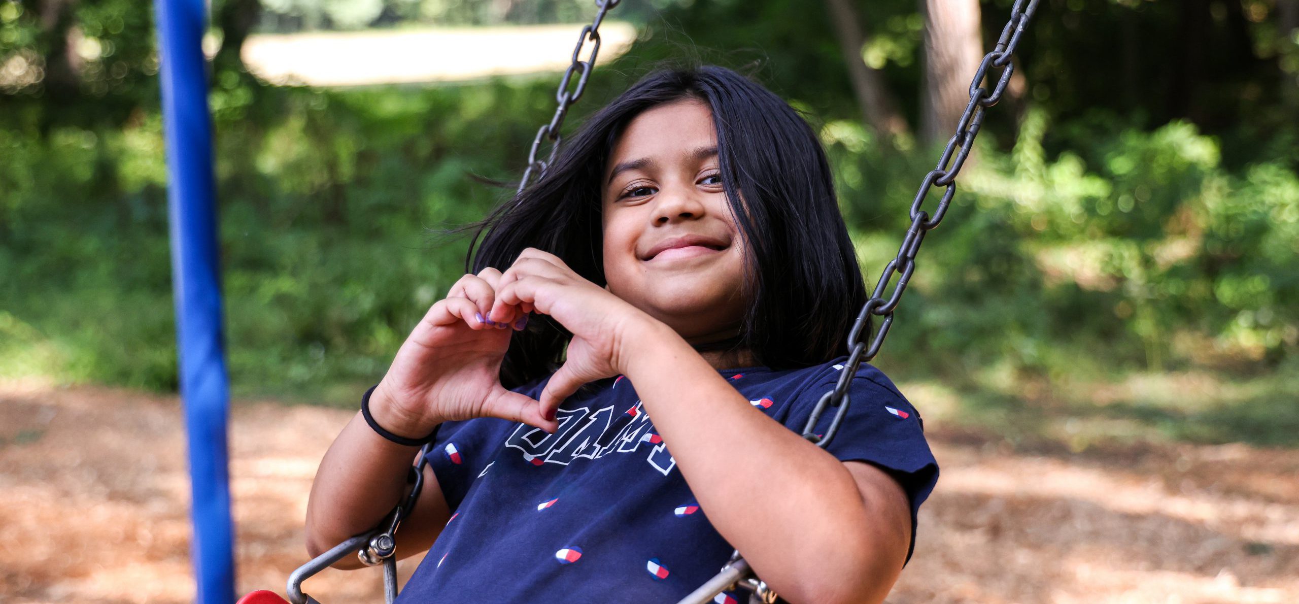 Student smiling and making heart-hands on the swings.