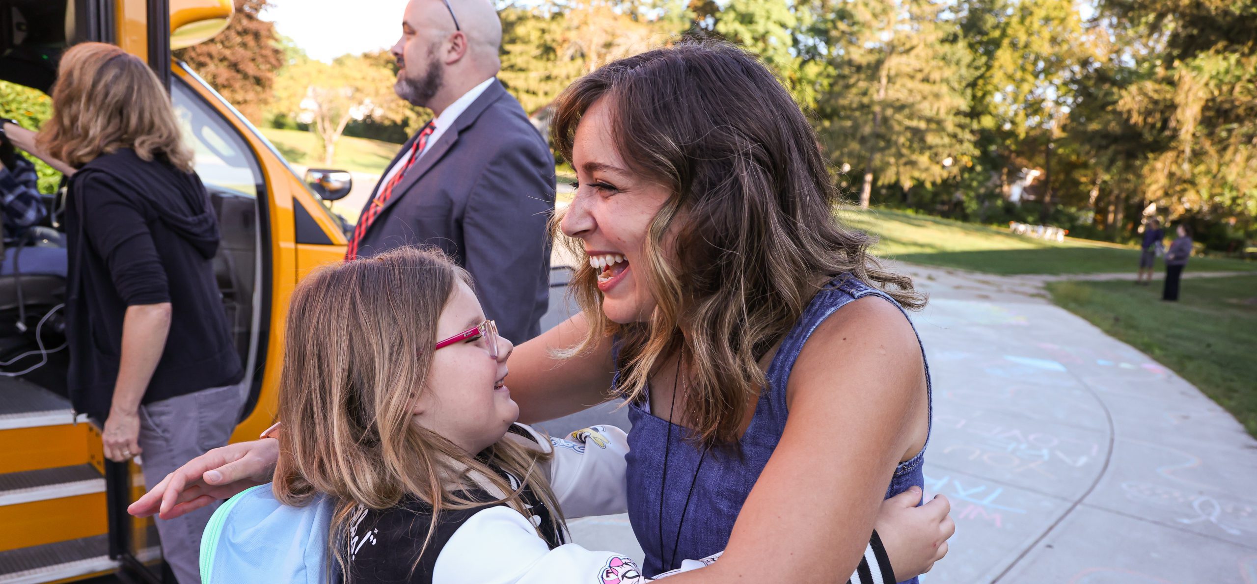 Elementary student hugging staff on first day of school. They are both smiling.