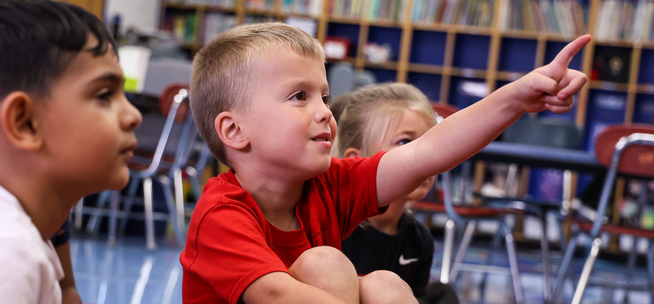 Elementary student learning in class with finger pointed up and smiling.