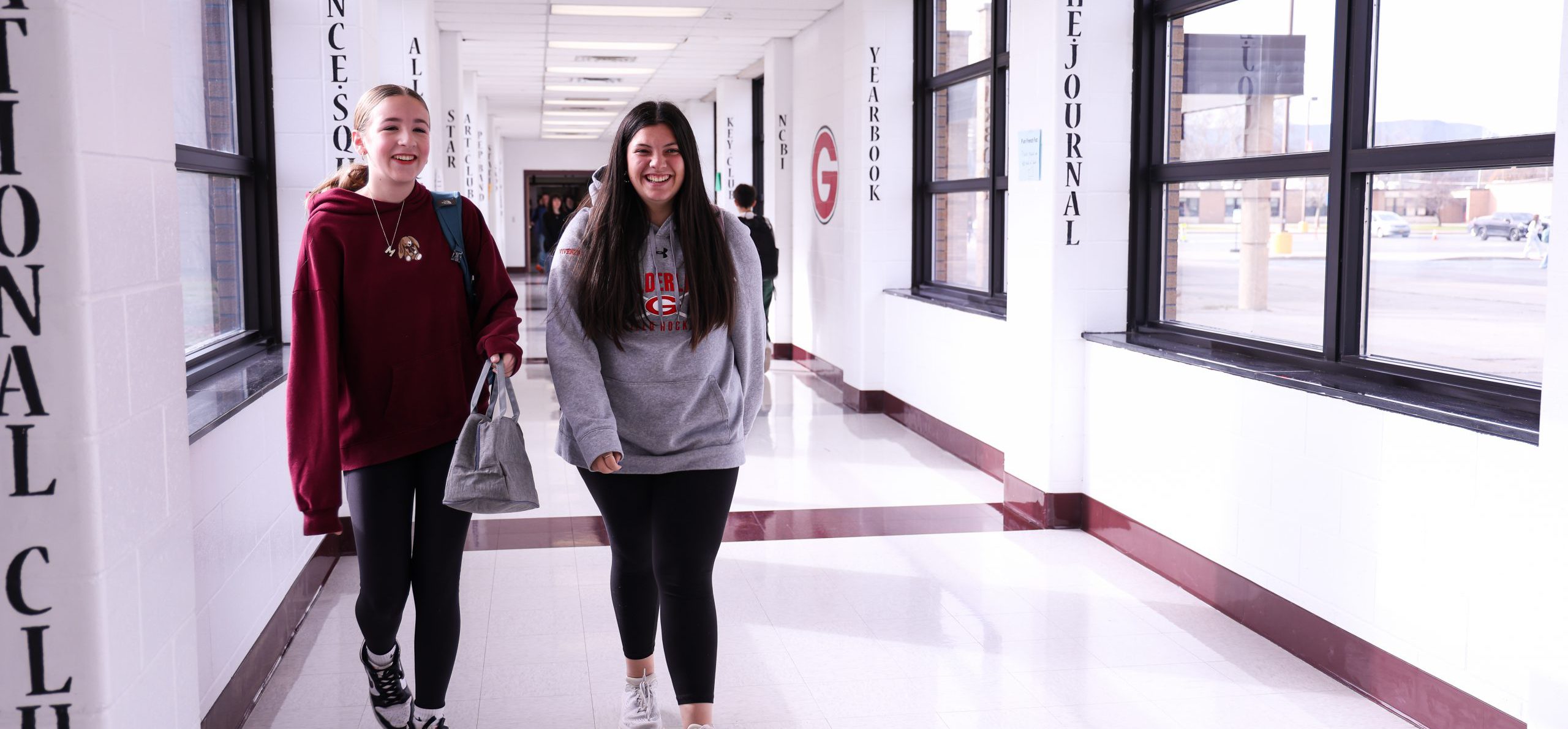 Two GHS students walking in a long hallway smiling.