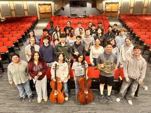 students standing in a theatre in between red seats with their instruments