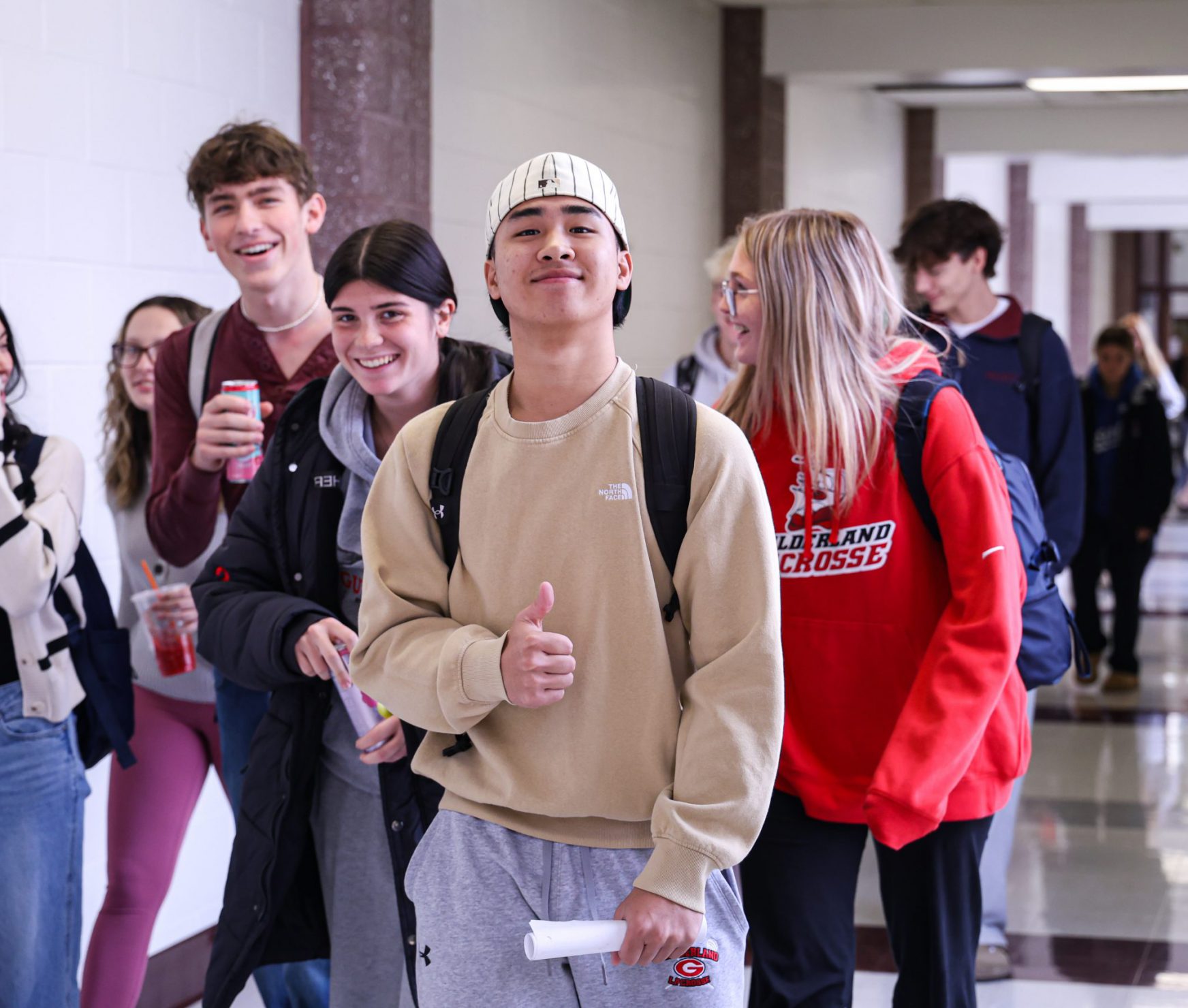Students smiling in the halls. One student is holding a thumbs up.