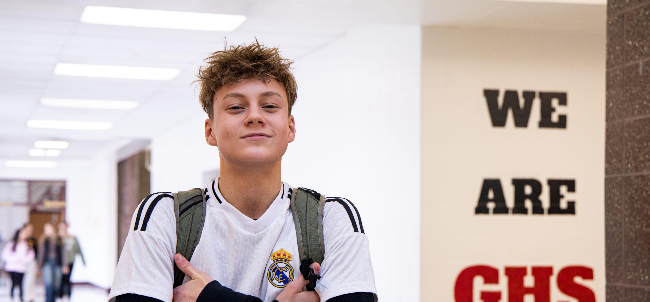 GHS student smiling in the halls. The text "We are GHS" is painted on the wall to the back right of the student.