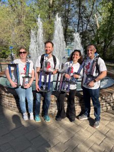four music instructors holding seven trophies in front of a fountain spouting water